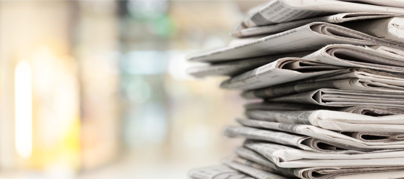 Stack of Newspapers Against Blurred Office
