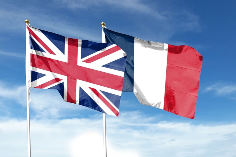 UK and French Flags Against Blue Cloudy Sky